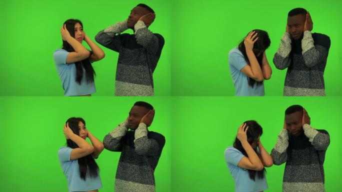 一名年轻的亚洲妇女和一名年轻的黑人男子从一个令人不快的声音-绿色屏幕工作室遮住耳朵