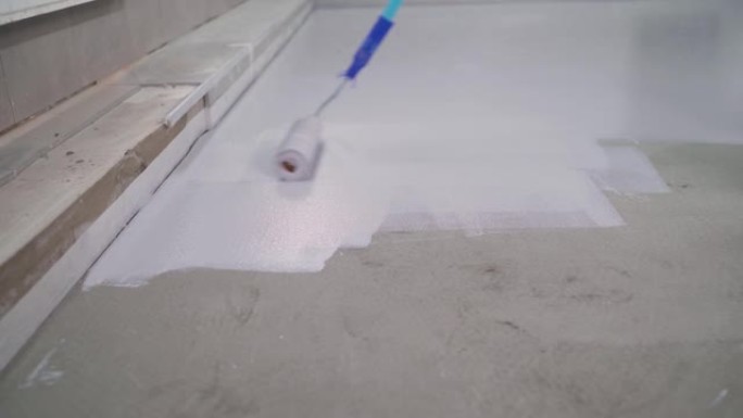 一名工人用白色油漆在混凝土地板上涂漆。一名工人用滚筒粉刷地板。用油漆滚筒手工喷漆白色地板防水
