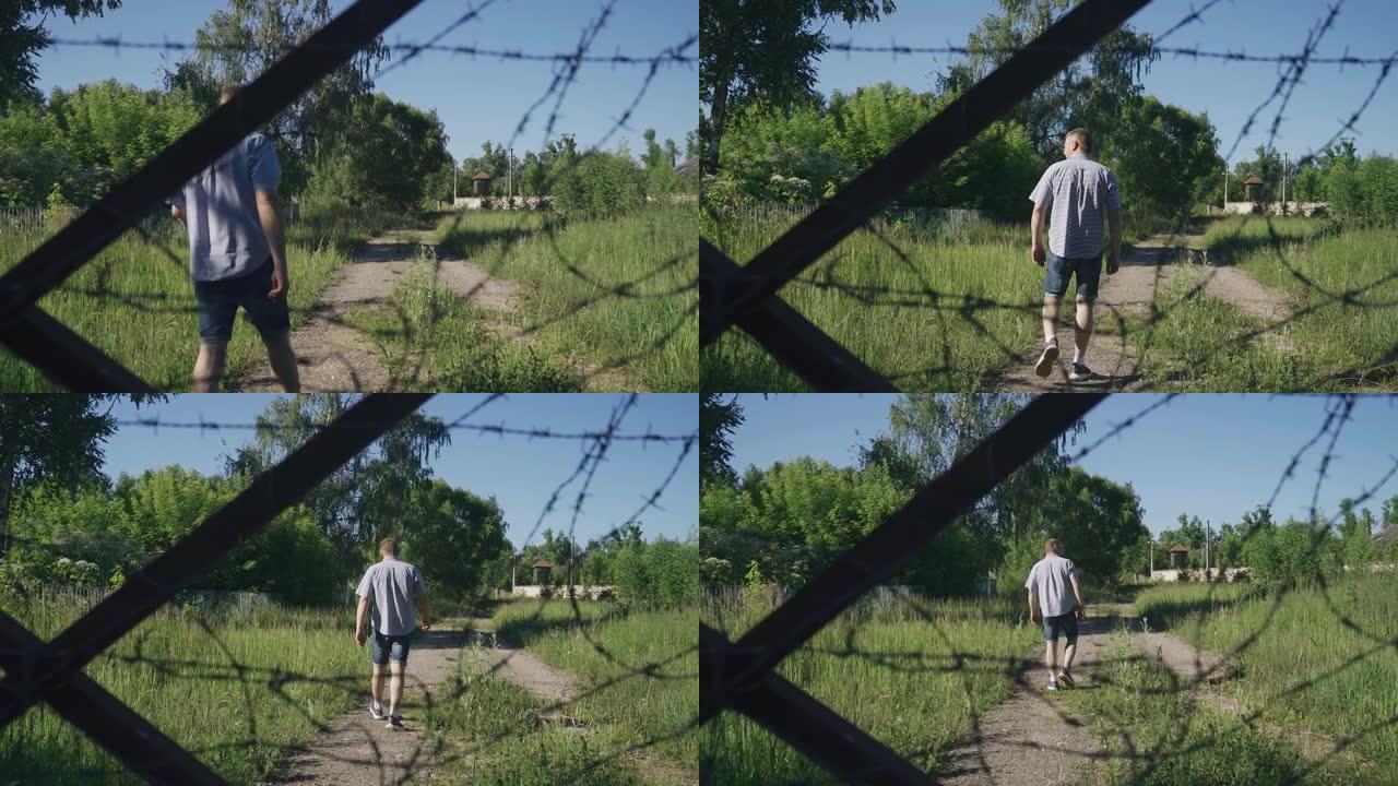 一个人走过一个废弃的禁区。穿过铁丝网围栏射击