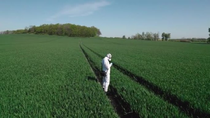 一名工人，一名身穿防护服的生物学家，脸上戴着口罩，穿过农田，背景是风力发电厂。