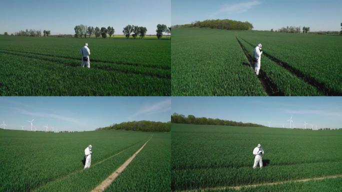 一名工人，一名身穿防护服的生物学家，脸上戴着口罩，穿过农田，背景是风力发电厂。