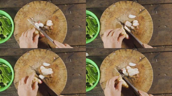 老亚洲人用刀子将高良姜切成薄片。准备制作食物菜单。泰国菜。顶视图。