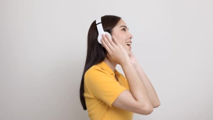 令人不寒而栗的亚洲女少年用白色耳机在与世隔绝的地方跳舞听音乐。穿着黄色衬衫的美丽年轻女子手触摸无线耳