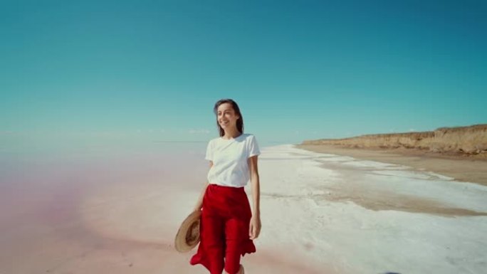 优雅的美女旅行者在亮粉色的湖盐平底鞋上快乐，女孩穿着红色长裙，手里拿着帽子