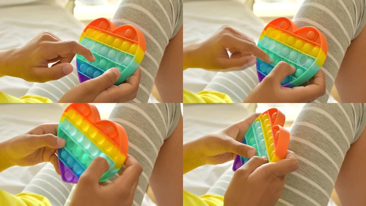 彩色抗压感觉玩具在孩子的手中坐立不安。女孩压在彩色彩虹柔软的硅胶泡泡上。压力和焦虑缓解。时髦的坐立不