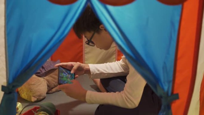 亚洲华裔青少年在家中舒适的照明帐篷中使用电话