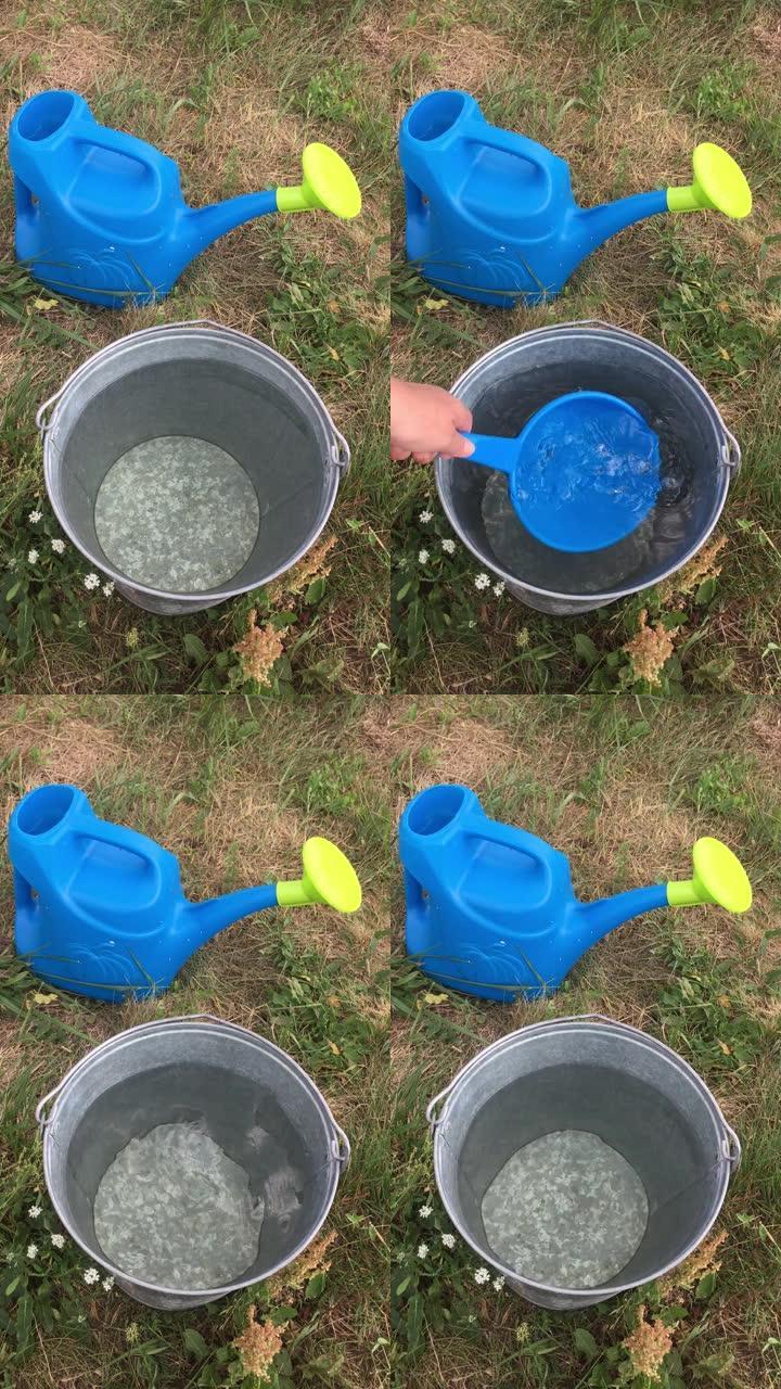 草地上的喷壶和一只手用金属桶里的塑料桶舀水