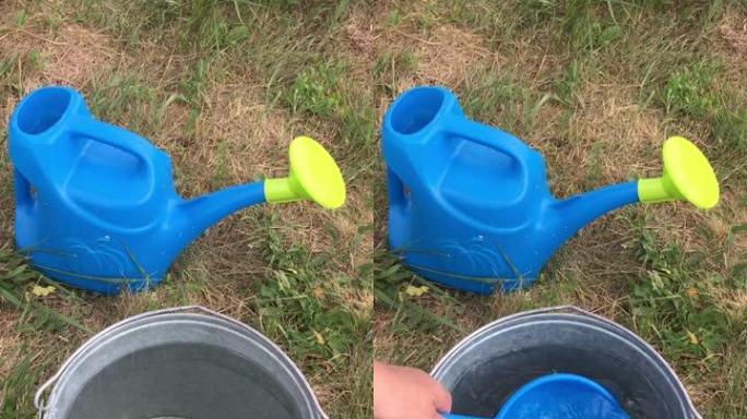 草地上的喷壶和一只手用金属桶里的塑料桶舀水