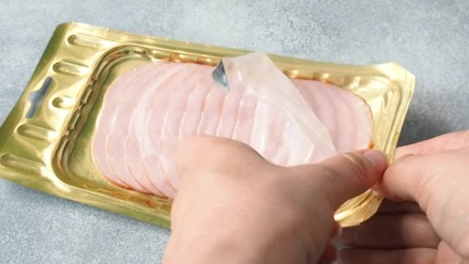 薄薄的猪肉火腿在真空包装中妇女双手打开包装。肉片碳酸盐包装，可长期储存