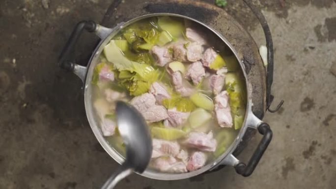 亚洲老太太在装满排骨，蔬菜，酸菜，香菜和葱的锅上搅拌汤。泰国菜菜单。顶视图。
