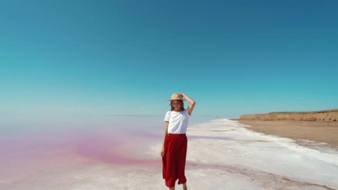 穿着红色裙子和草帽的旅游女人在粉色湖享受夏季旅行，在盐滩边散步