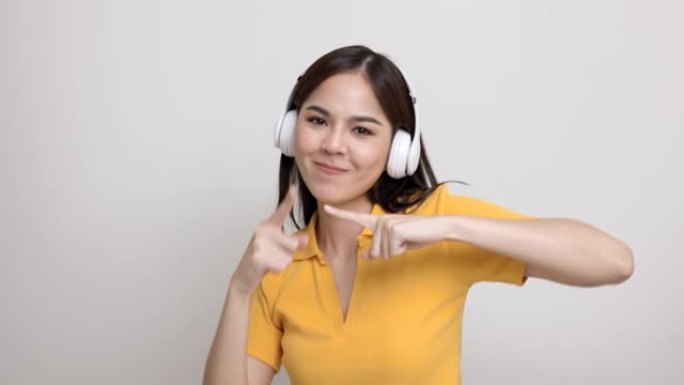 可爱的亚洲女少年在与世隔绝的情况下用白色耳机听音乐。穿着黄色衬衫的美丽年轻女子手触摸无线耳机，在房间
