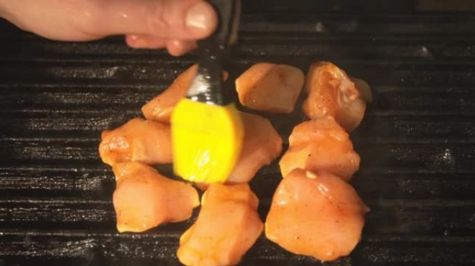 厨师用刷子和黄油将烧烤的鸡肉片润滑。