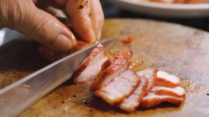 有人用刀切红色烤猪肉。准备烹饪中国菜单。熟肉。面条。