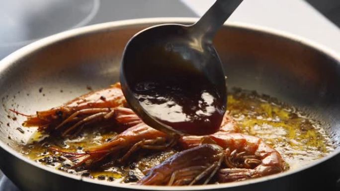 用勺子的酱汁将虾倒在烤架上。大虾在平底锅里煎炸的特写镜头。厨师在热锅上煎皇家虾。宏观海洋食品制备