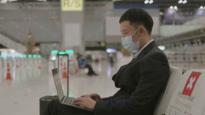 戴着防护面罩的亚洲精力充沛的商人在等待飞机抵达时专注于工作-库存视频