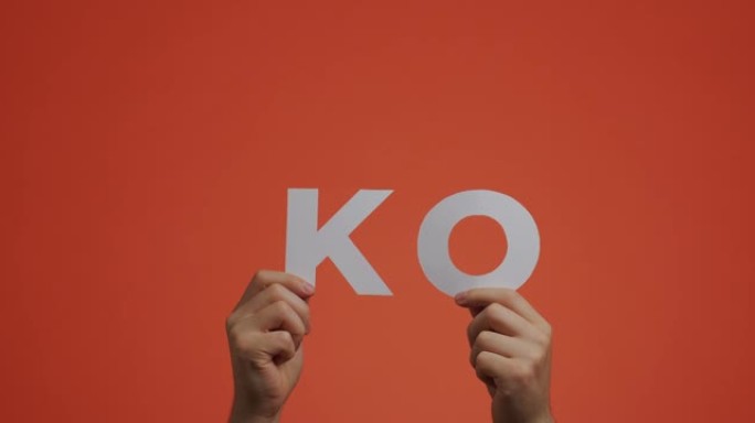 手显示英语单词KO。男子为博客展示了用雕花纸制成的淘汰赛标志