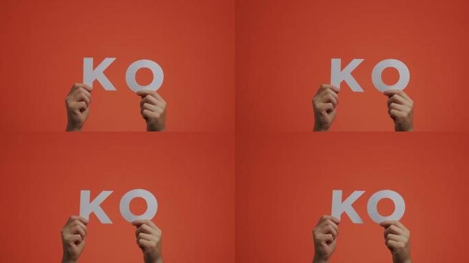 手显示英语单词KO。男子为博客展示了用雕花纸制成的淘汰赛标志