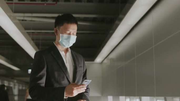 带防护面罩的亚洲中型成人商人在飞行前用智能手机检查出发时间和入住时间