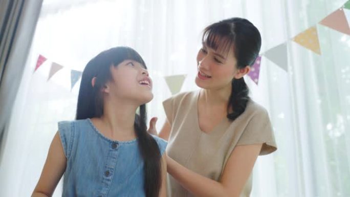 亚洲慈爱的母亲和年轻的小女孩女儿在家里的客厅里度过闲暇时光。有爱心的妈妈用温和的发刷梳理小孩的头发。