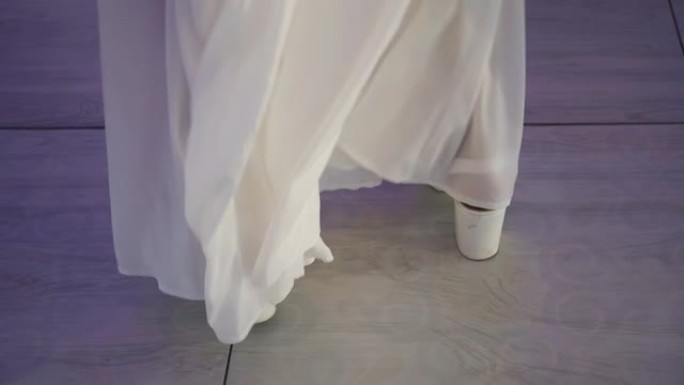 一个穿着白色长裙和鞋子的女孩在舞池里跳舞。射击女孩的腿