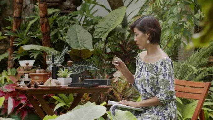 一个女人在阴凉的花园里喝着咖啡，读杂志。