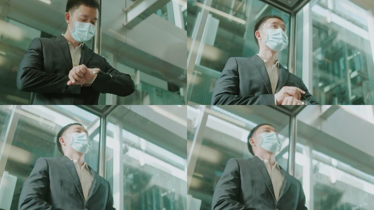 戴着防护口罩的亚洲中年商人在电梯里看手表，准备去机场办理登机手续-股票视频