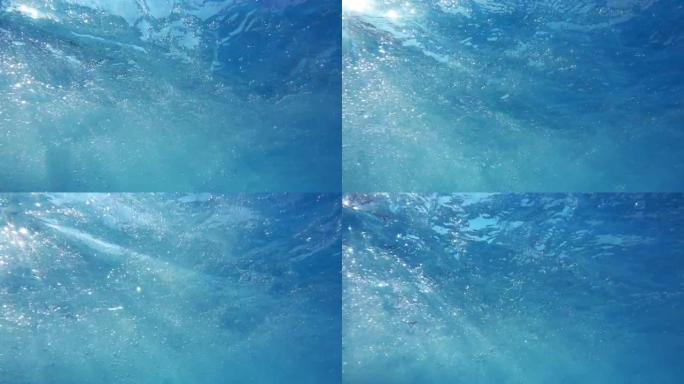 就在水面电影的下方，波浪，涟漪，气泡和太阳光线穿过水面
