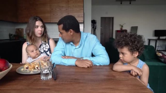 有两个孩子的混血家庭坐在家里的餐桌旁