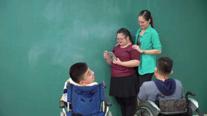 十几岁的唐氏综合症女孩练习演讲，在数字平板电脑上阅读演讲，残疾的小学生小组坐在轮椅上，亚洲美女老师站