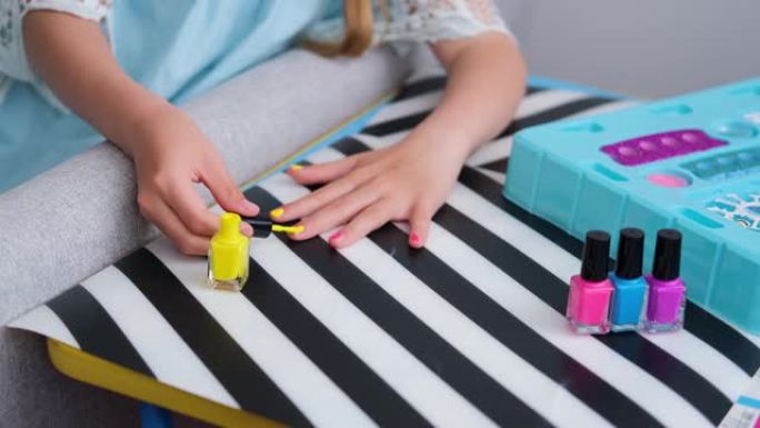 孩子坐在桌前，用亮黄色的指甲油涂指甲。一个小女孩修指甲。美容院游戏。孩子们的乐趣。