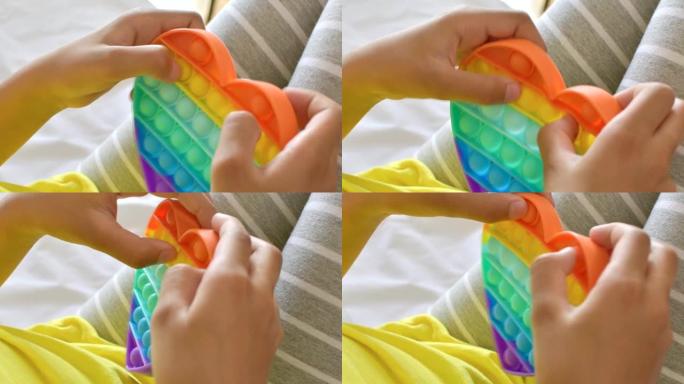 彩色抗压感觉玩具在孩子的手中坐立不安。女孩压在彩色彩虹柔软的硅胶泡泡上。压力和焦虑缓解。时髦的坐立不