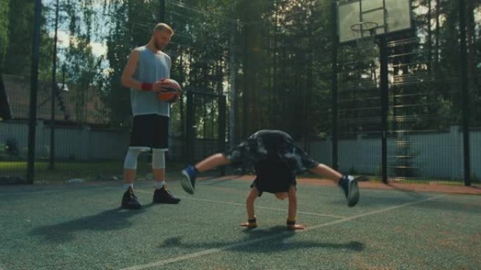 篮球运动员。体育家庭。童子秀倒立与父亲在阳光下的篮球场上锻炼