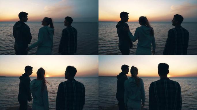 在夕阳背景下站在海边的三个年轻人