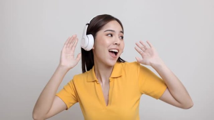 开朗的亚洲女少年在与世隔绝的情况下用白色耳机听音乐。穿着黄色衬衫的美丽年轻女子手触摸无线耳机，在房间