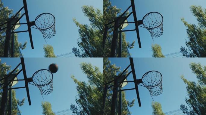 大自然的篮球场。扔进篮球圈的球在夏天的天空背景下飞过。瞄准、目标概念
