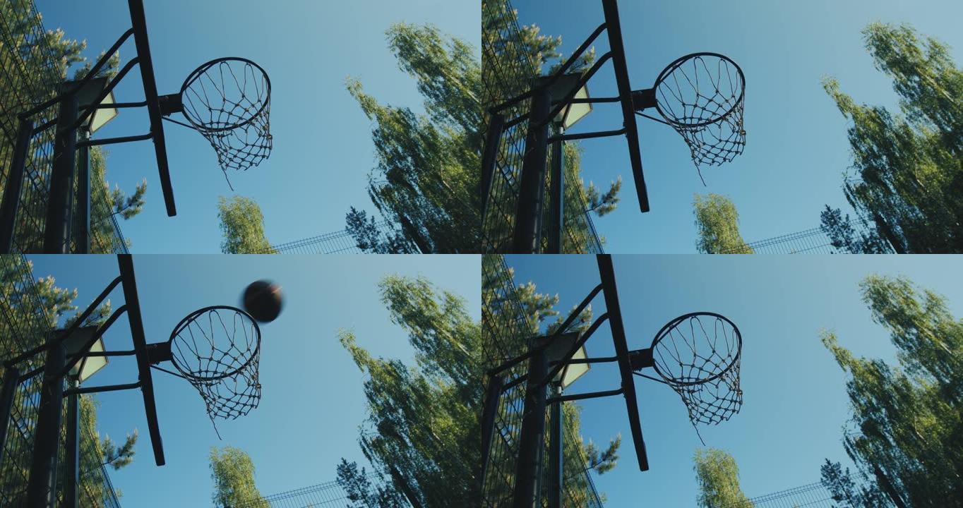 大自然的篮球场。扔进篮球圈的球在夏天的天空背景下飞过。瞄准、目标概念