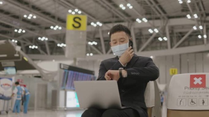 亚洲充满活力的商人，戴着防护口罩，拿起电话，在等待飞机抵达机场期间从合作伙伴那里获取有关新想法的信息