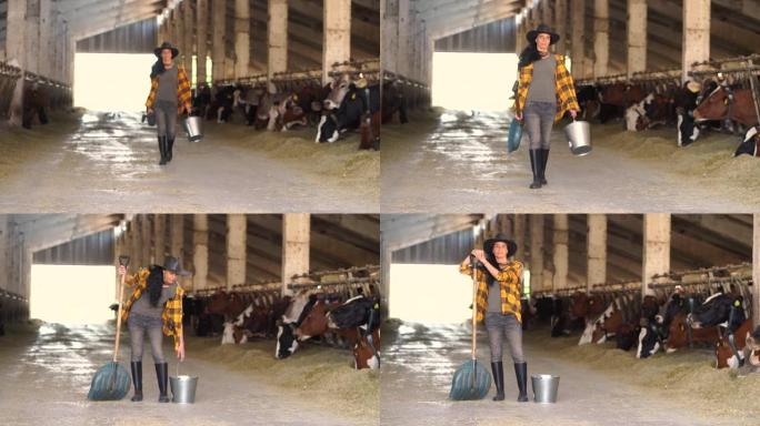 4k视频宽镜头，女农场工人拿着水桶和铁锹在农场牛棚里行走
