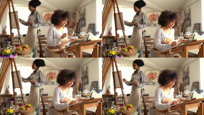 4k视频两名漂亮的美国黑人年轻女性在工作室里画画，看着画，微笑着