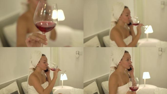 穿着白毛巾的模糊年轻女子在床上品尝红酒