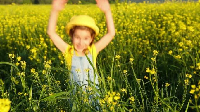 一个戴着黄色帽子的女孩躲在高高的草丛中，在夏日盛开的田野里，在阳光下跳了出来。夏季，日落，假期，防晒