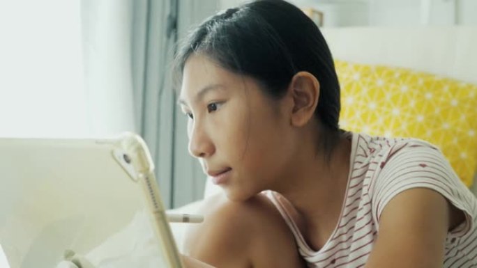 亚洲女孩在家里的地板上用数字平板电脑画画，在家上学的生活方式概念。