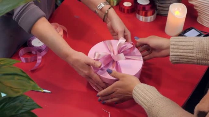 客户在礼品店买带丝带的礼品盒。卖家在车间赠送粉色圆盒，用于浪漫礼物，带粉色胶带。