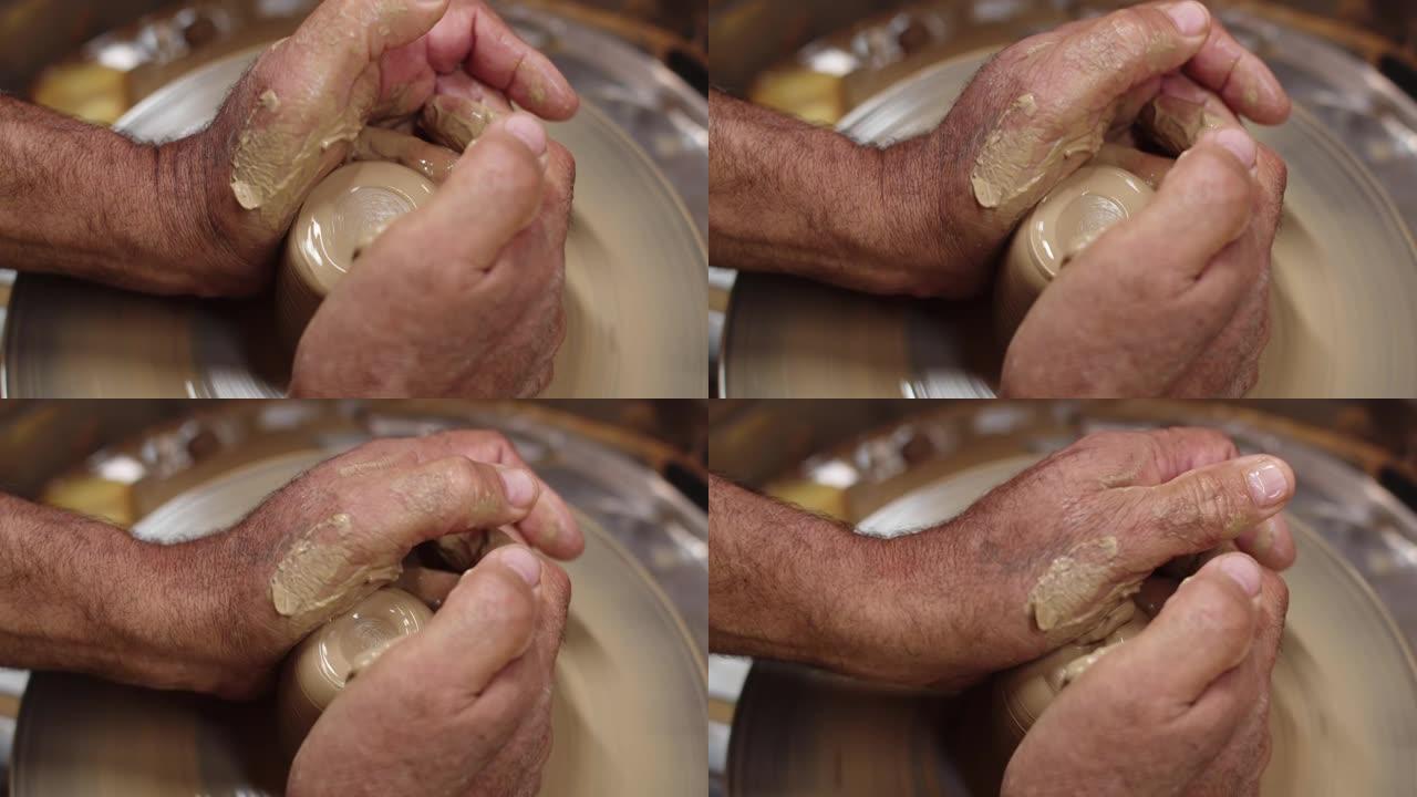 波特的男性手向下压在波特的轮子上旋转的粘土片，使其具有不同的形状，特写。工匠在他的车间里用粘土工作