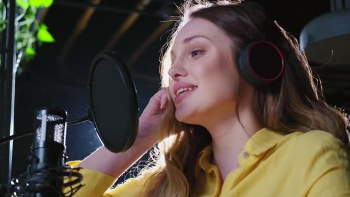 戴着耳机的女人在唱片工作室的麦克风中唱歌