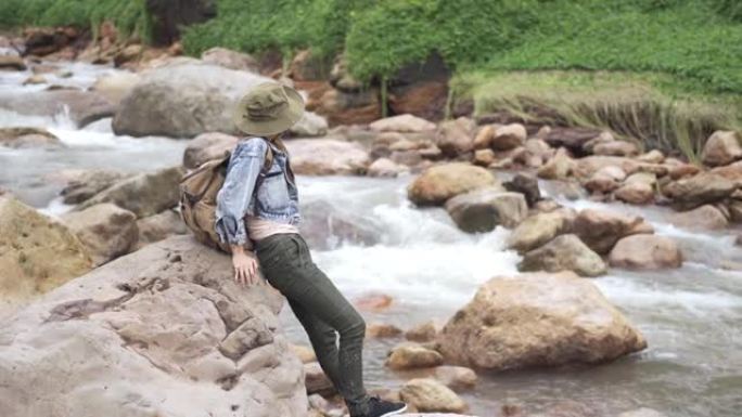 4k亚洲女子坐在溪边的岩石上