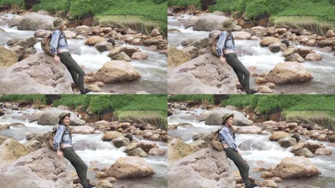 4k亚洲女子坐在溪边的岩石上
