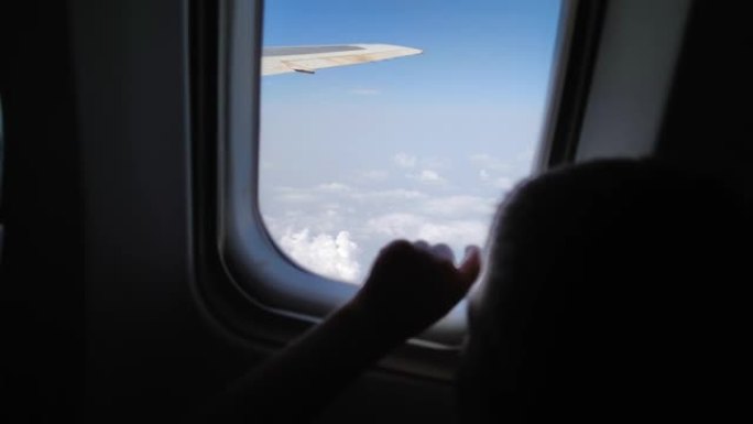 飞机上的儿童乘客在窗外飞来飞去，窗外风景优美，好奇的小男孩在飞行过程中在玻璃上抚摸手指