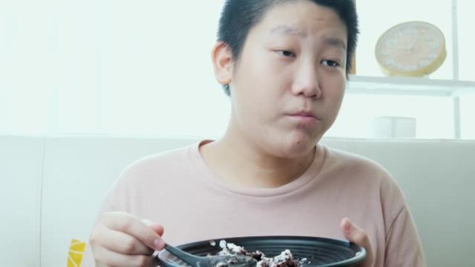 亚洲男孩在家沙发上吃美味的巧克力蛋糕，生活方式理念。